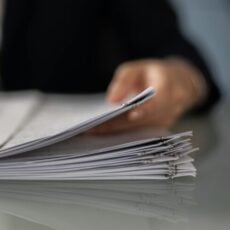 Blurred hand holding a stack of documents on a glass desk with focus on papers.